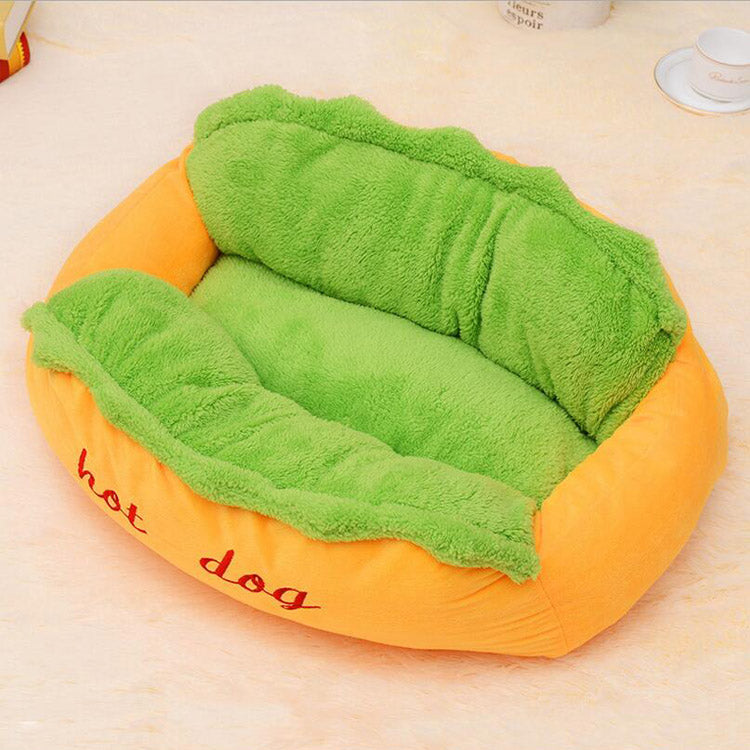 Hot dog shaped pet bed with orange bun and green lettuce fleece, angled studio view